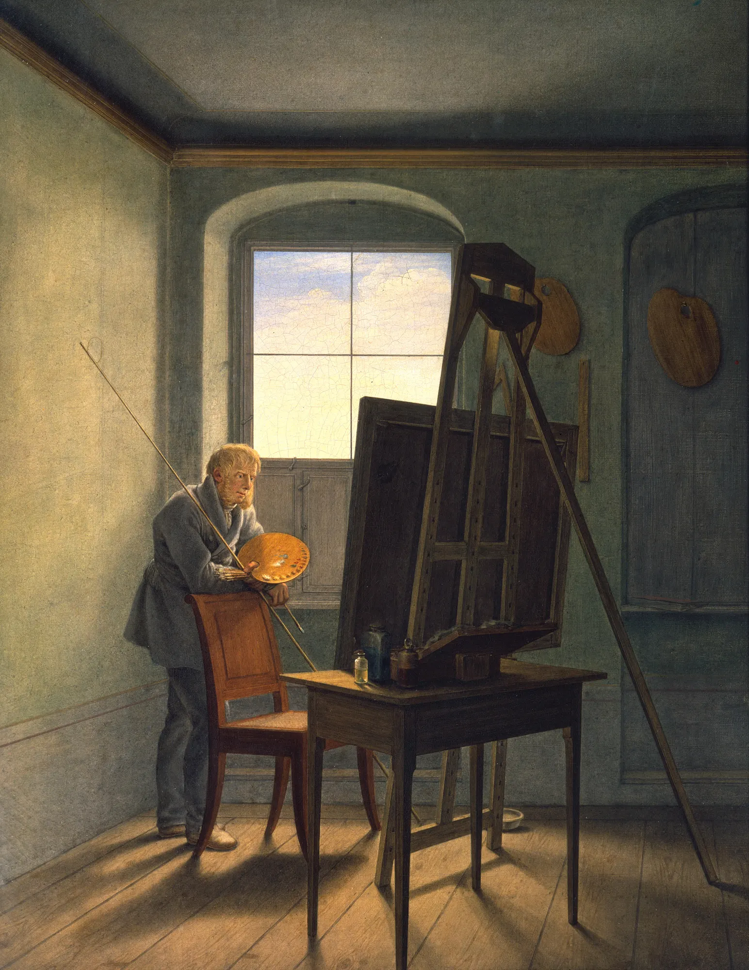 The painter alone at his easel in an almost empty studio, seen from behind, lit by one tall half-shuttered window.