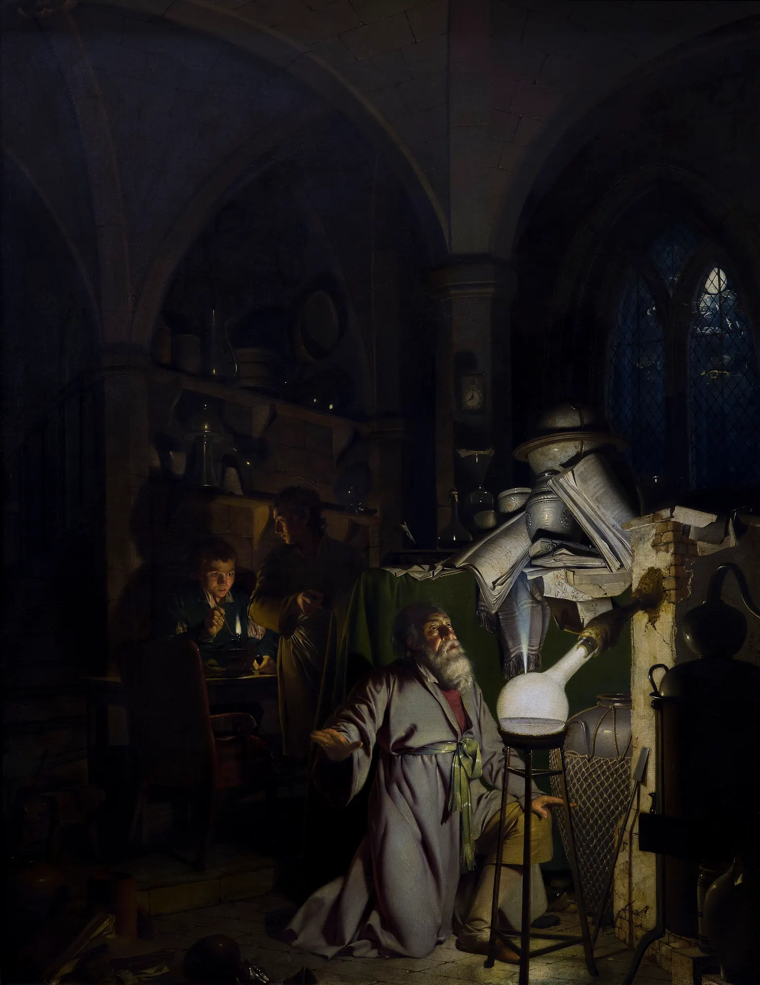 An alchemist kneels in his vaulted workshop as the vessel before him erupts in white light, two apprentices at their work in the shadows behind.